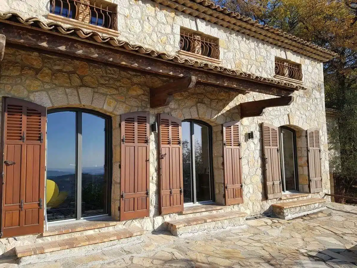 Menuiseries mixtes bois/alu Finstral à cintre plat installées à Saint-Jeannet. Une alliance réussie entre charme de la pierre et performance moderne, offrant luminosité et élégance à une façade provençale authentique.